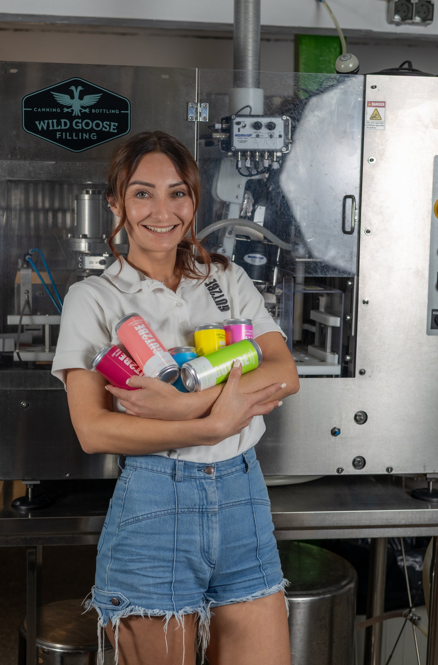 A GUT2BE kombucha gyártója színes GUT2BE kombucha dobozokat tart a karjában a palackozóüzemben